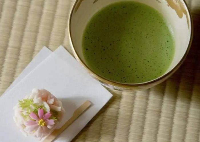 A frothy cup of matcha on a tatami mat; next to it, a beautiful wagashi sweet.